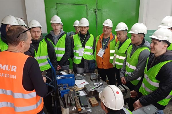 Uczniowie w odzieży ochronnej w zakładzie